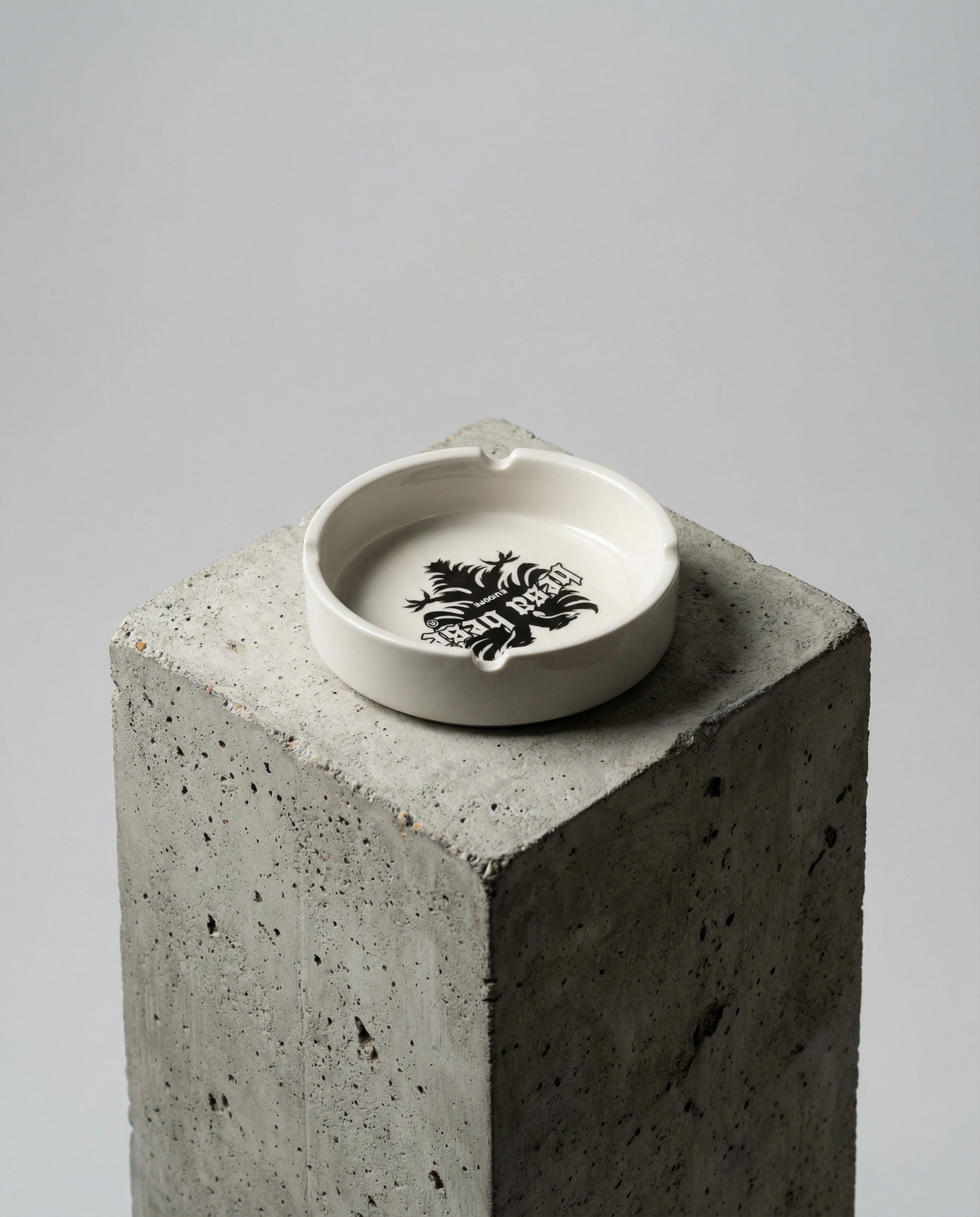 Ceramic ashtray with a logo on a concrete block against a gray background