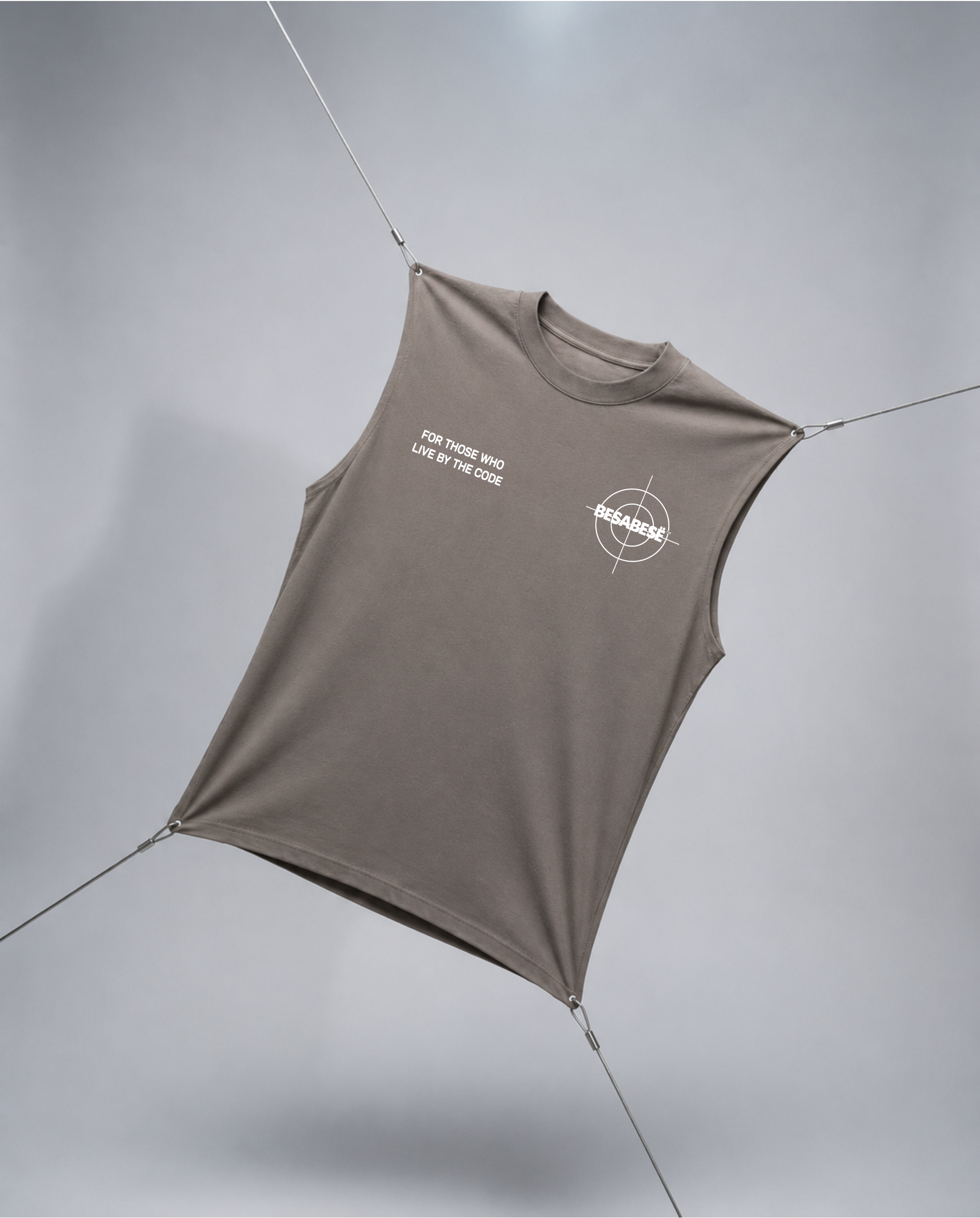 A sleeveless fitted tank top in taupe-brown with white printed graphics on the chest, suspended by thin cords against a light gray studio background.